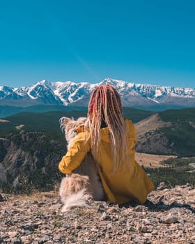 Women with pink dreads and the dog enjoy the stunning view on a snowy mountains peaks and Aktru glacier. Beautiful landscape of Altay region, Russia.