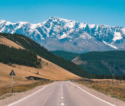 Empty asphalt road in front of huge majestic mountains with snow covered peaks. Beautiful landscape of Altay region, Russia.