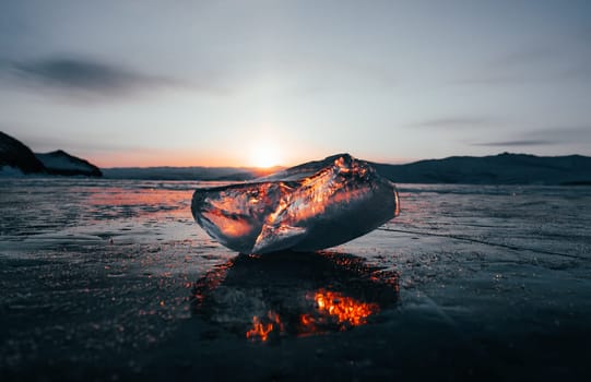 Ice crystal on the frozen surface of Lake Baikal in early morning. Sky and sun reflections on the ice surface. Amazing winter landscape. Winter tourist season at lake Baikal