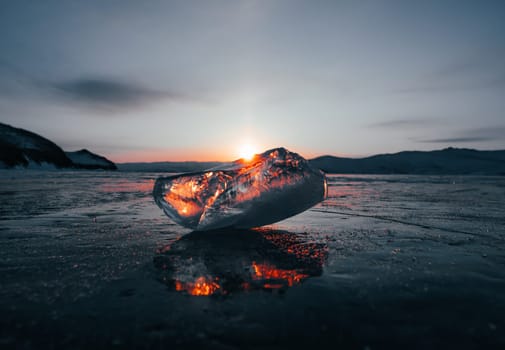 Ice crystal on the frozen surface of Lake Baikal in early morning. Sky and sun reflections on the ice surface. Amazing winter landscape. Winter tourist season at lake Baikal