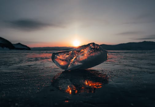 Ice crystal on the frozen surface of Lake Baikal in early morning. Sky and sun reflections on the ice surface. Amazing winter landscape. Winter tourist season at lake Baikal