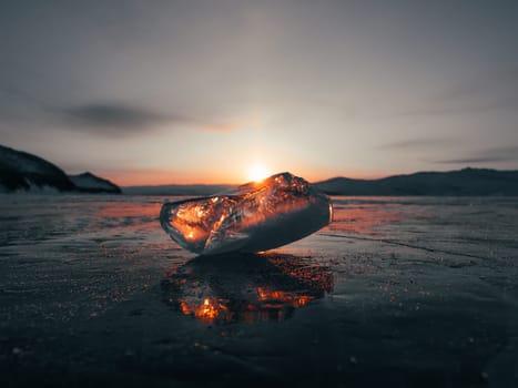 Ice crystal on the frozen surface of Lake Baikal in early morning. Sky and sun reflections on the ice surface. Amazing winter landscape. Winter tourist season at lake Baikal