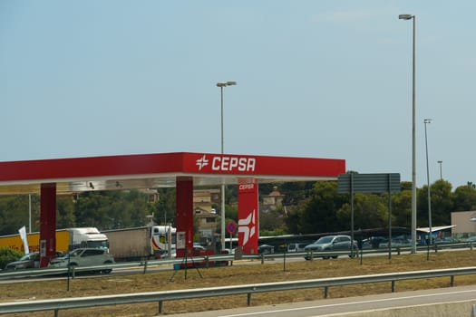 Barcelona, Spain - May 24, 2023: A gas station CEPSA sits on the side of a busy road, with cars refueling and passing by on their journeys. The station is equipped with pumps, signs, and convenience store items.