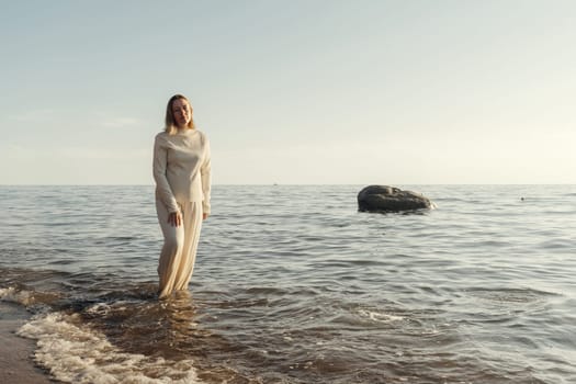 A woman standing waist-deep in the water at a sandy beach, with waves gently splashing around her.