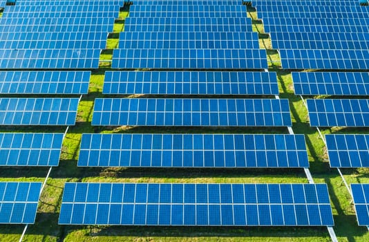 Aerial close-up view of Solar Panels Farm with sunlight. Flying over the solar power plant at sunny day. Renewable energy power plant producing sustainable clean solar energy from the sun.