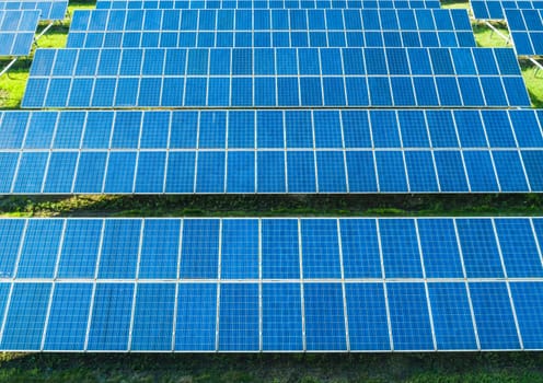 Aerial close-up view of Solar Panels Farm with sunlight. Flying over the solar power plant at sunny day. Renewable energy power plant producing sustainable clean solar energy from the sun.