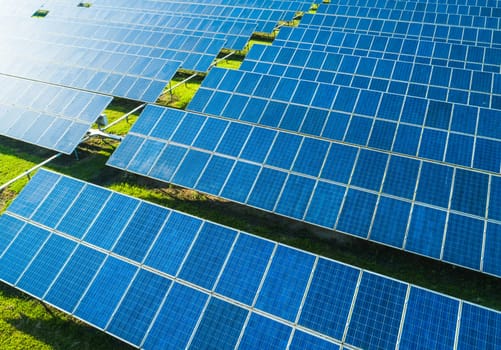 Aerial close-up view of Solar Panels Farm with sunlight. Flying over the solar power plant at sunny day. Renewable energy power plant producing sustainable clean solar energy from the sun.