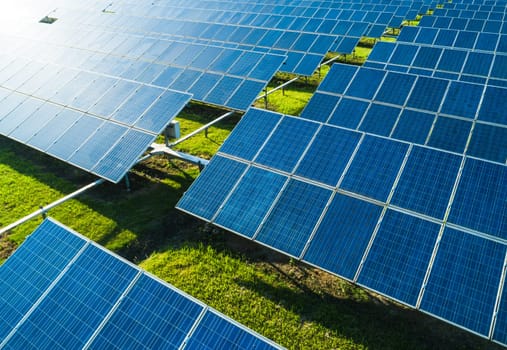 Aerial close-up view of Solar Panels Farm with sunlight. Flying over the solar power plant at sunny day. Renewable energy power plant producing sustainable clean solar energy from the sun.