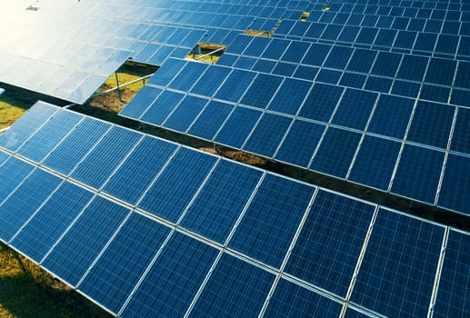 Aerial close-up view of Solar Panels Farm with sunlight. Flying over the solar power plant at sunny day. Renewable energy power plant producing sustainable clean solar energy from the sun.