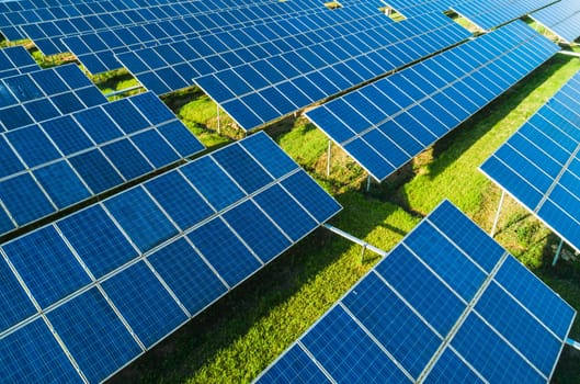 Aerial close-up view of Solar Panels Farm with sunlight. Flying over the solar power plant at sunny day. Renewable energy power plant producing sustainable clean solar energy from the sun.