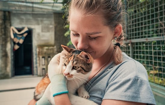 Female volunteer holds on hands cat in shelter