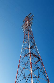 Bottom view of a high-voltage electricity pylon against blue sky at sunny day. High-voltage power transmission tower. Power engineering.