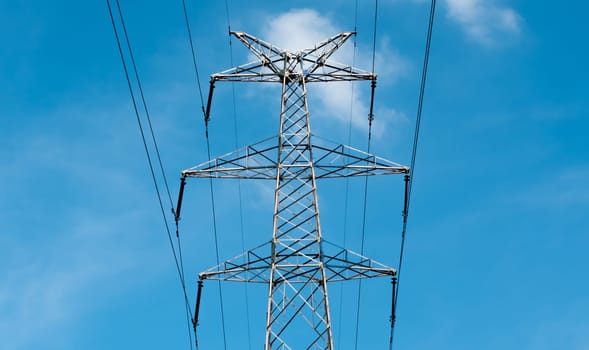 Bottom view of a high-voltage electricity pylon against blue sky with clouds at sunny day. High-voltage power transmission tower. Power engineering.