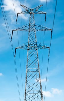 Bottom view of a high-voltage electricity pylon against blue sky with clouds at sunny day. High-voltage power transmission tower. Power engineering.