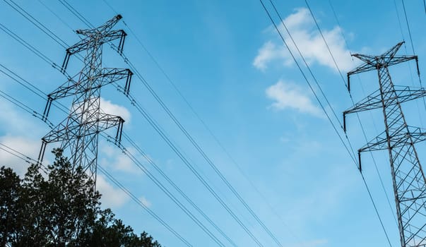 Bottom view of a high-voltage electricity pylons against blue sky with clouds at sunny day. High-voltage power transmission towers. Power engineering.