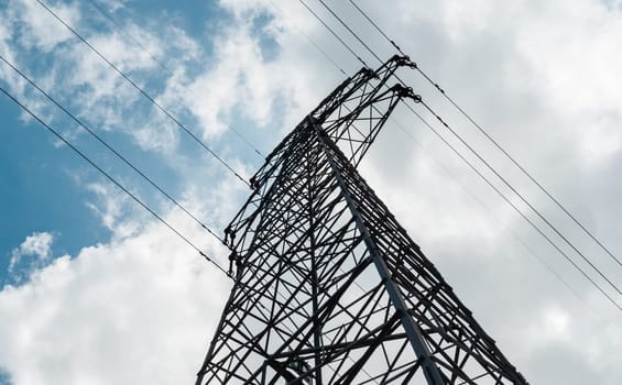 Bottom view of a high-voltage electricity pylon against blue sky with clouds at sunny day. High-voltage power transmission tower. Power engineering.