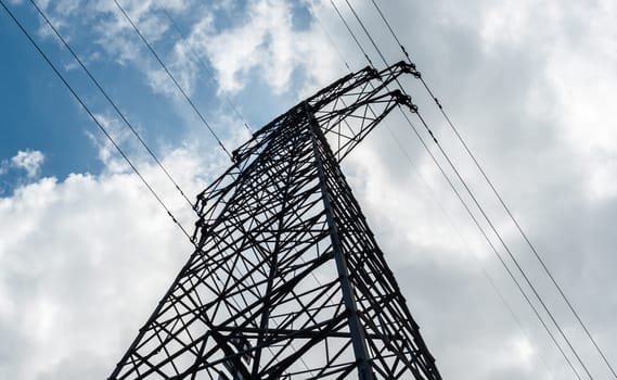 Bottom view of a high-voltage electricity pylon against blue sky with clouds at sunny day. High-voltage power transmission tower. Power engineering.