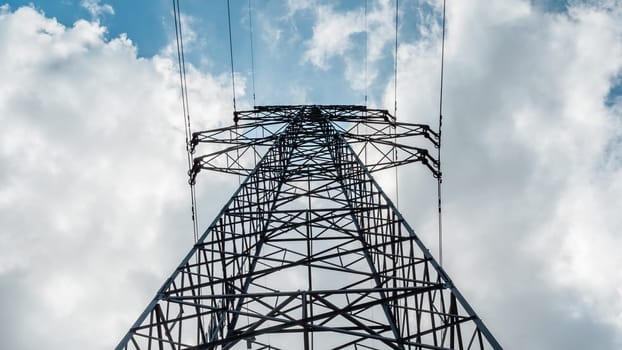 Bottom view of a high-voltage electricity pylon against blue sky with clouds at sunny day. High-voltage power transmission tower. Power engineering.