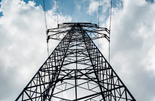 Bottom view of a high-voltage electricity pylon against blue sky with clouds at sunny day. High-voltage power transmission tower. Power engineering.