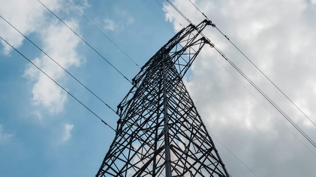 Bottom view of a high-voltage electricity pylon against blue sky with clouds at sunny day. High-voltage power transmission tower. Power engineering.