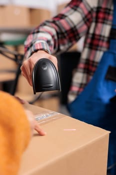 Warehouse employee scanning cardboard box barcode while doing inventory control. Delivery service operator managing parcel receiving and checking qr code with scanner close up