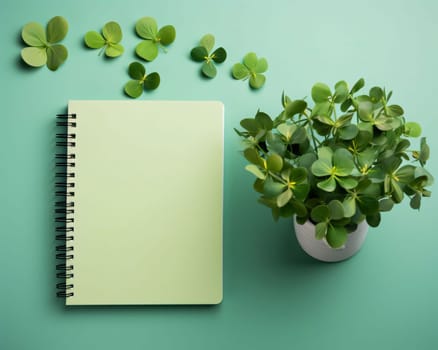 Notebook with a bright blank page, next to a pot with green limbs around scattered clovers. Space for your own content. Green four-leaf clover symbol of St. Patrick's Day. Happy time of celebration in green color.