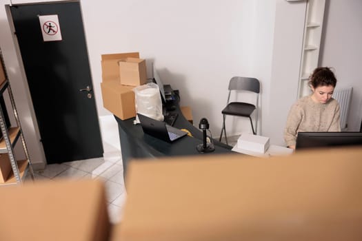 Top view of supervisor standing at counter desk, analyzing merchandise logistics on computer. Storage room worker checking clients online orders preparing packages for delivery