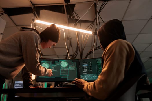 Hackers team hacking online server, stealing data, cybercrime. Cyberattack, it specialist pointing at code on pc screen, criminals programming internet virus at night time