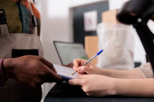 Storage room supervisor signing delivery documents, african american employee working at customers orders preparing packages in storehouse. Diverse team standing at counter in warehouse. Close up