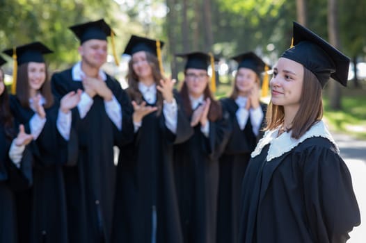 Group of happy students in graduation gowns outdoors. A young girl in the foreground