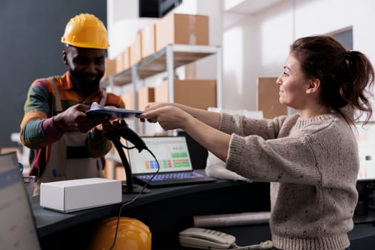 African american employee signing inventory report, discussing customers online orders before start preparing packages in warehouse. Supervisor standing at counter desk checking goods logistics