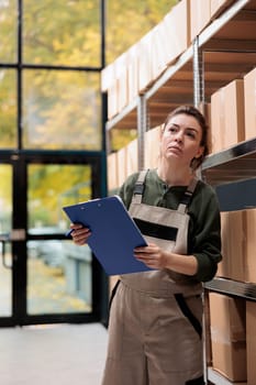 Stockroom employee supervising cardboard packages in mail sorting center and writing inventory clipboard. Post office warehouse manager searching customer parcel, checking postal form.