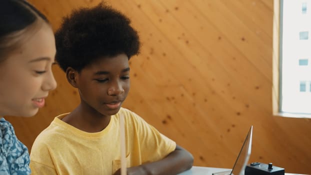 Site view of african boy and caucasian girl in casual cloth working together to coding prompt or programing system at table with laptop and electronic equipment at STEM technology class. Edification.