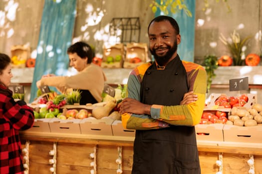 Farmers market vendor selling healthy organic products next to food marketplace stall. Young man with seasonal locally grown vegetables and fresh natural fruits and vegetables.