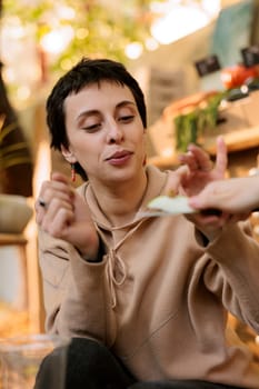 Young woman customer in selective focus, tasting fresh organic green apple while shopping at outdoor farmers market. Before purchasing, a female client samples locally grown organic fruits.