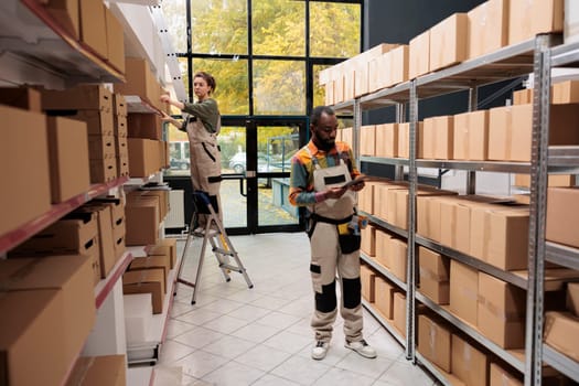 African american manager analyzing orders checklist before start preparing customers packages for delivery. Storage room manager working with cardboard boxes during goods quality control
