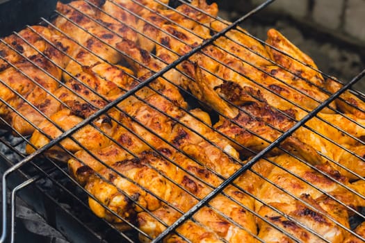 Delicious chicken frying on barbecue grill grate outdoor. Seasoning falling on fresh grilled chicken wings. Summer party food ideas. BBQ Juicy roasting chicken grill legs on grill grate