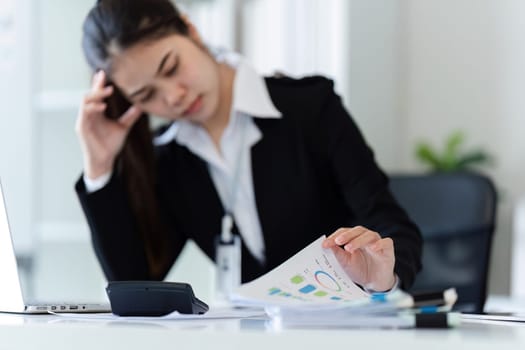 A woman is sitting at a desk with a laptop and a pen. She is writing something on a piece of paper