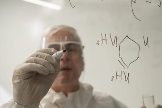 An elderly Caucasian male chemist in a protective suit writes on glass