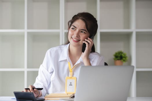 Business Caucasian woman Talking on the phone and using a laptop with a smile while sitting at modern office.