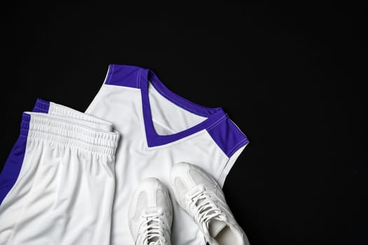 A white and purple basketball jersey and matching shorts are neatly placed beside a basketball and a pair of white sneakers, all set against a dark backdrop. The arrangement suggests preparation for a game or practice session.