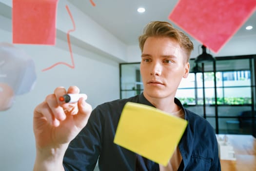 Professional caucasian businessman writing marketing idea by using mind map and sticky notes on glass board at modern meeting room. Creative business and planing concept. Closeup. Immaculate.