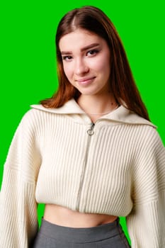 A young woman stands confidently against a vivid green background, dressed in a casual yet fashionable white cropped hoodie and a gray pleated skirt. Her expression is serene with a hint of contemplation, and her body language exudes a relaxed poise.