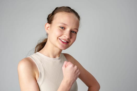 Young Woman in Casual Attire Smiling and Making a Fist Pump Gesture on a Plain Background close up