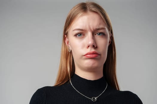 Young Woman In Black Shirt Expressing Discontent Against Grey Background close up