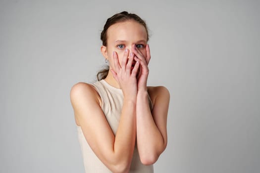 Young Woman Covering Her Face With Her Hands in Fear on gray background close up