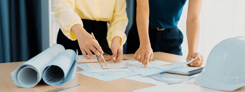 Professional architect team used divider measure during draft blueprint on table with architectural document, safety helmet and blueprint scatter around. Closeup. Focus on hand. Delineation.