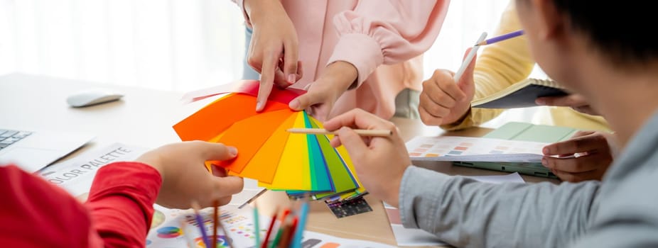 Cropped image of professional designer pick up the color at meeting at meeting table with color palette and document scatter around. Creative design and teamwork concept. Closeup. Variegated.