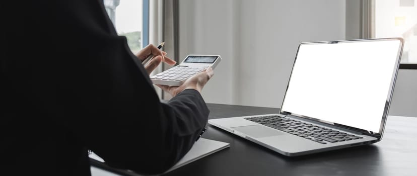 Close up Business woman using calculator and laptop for do math finance on wooden desk in office and business working background, tax, accounting, statistics and analytic research concept.