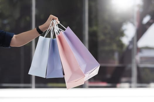 A person is holding four shopping bags, one of which is pink. The bags are being held in a way that suggests they are being carried by a person who is either shopping or has just finished shopping